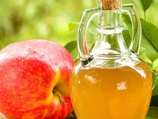 A bottle of apple cider vinegar next to fresh apples