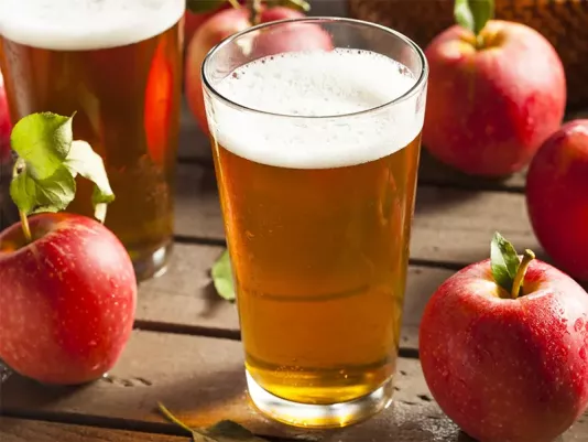 Homemade apple cider in a clear glass, surrounded by ripe apples