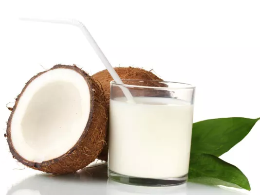 A glass of coconut milk next to a fresh coconut