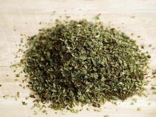 Dried oregano in a transparent jar next to a wooden spoon