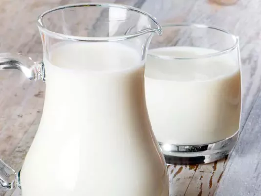 A glass of fresh milk on the table next to a jug