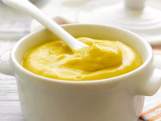 A jar of yellow mustard and a spoon of sauce