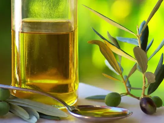 A bottle of olive oil next to fresh olives on a table