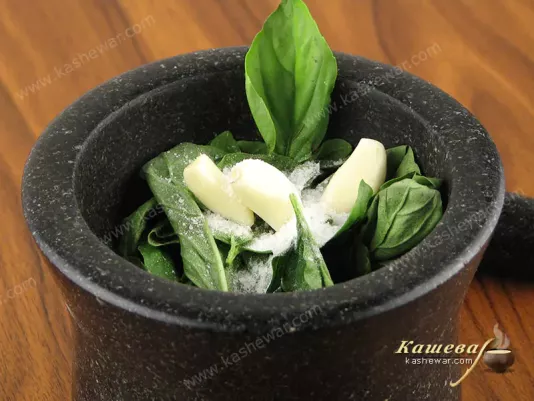 Grinding pesto sauce ingredients in a mortar
